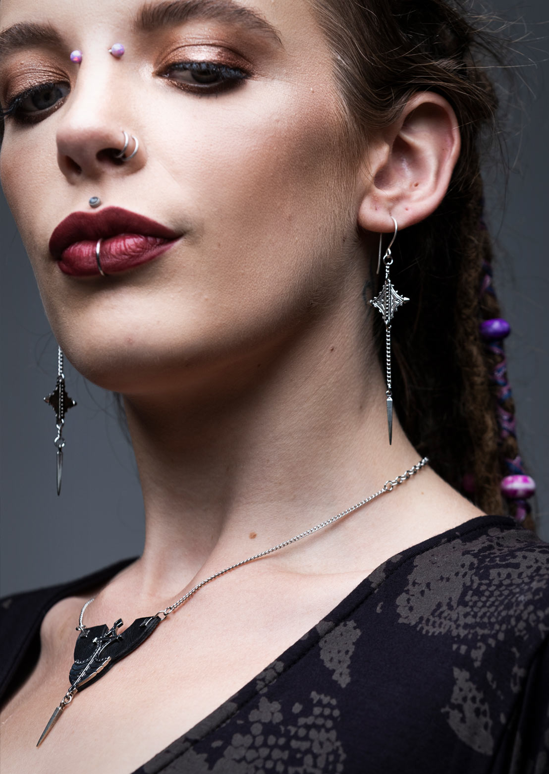 A person wearing a pair of twin earrings with diamond-shaped brass ornaments and sterling silver hooks, from the Nubian Collection.