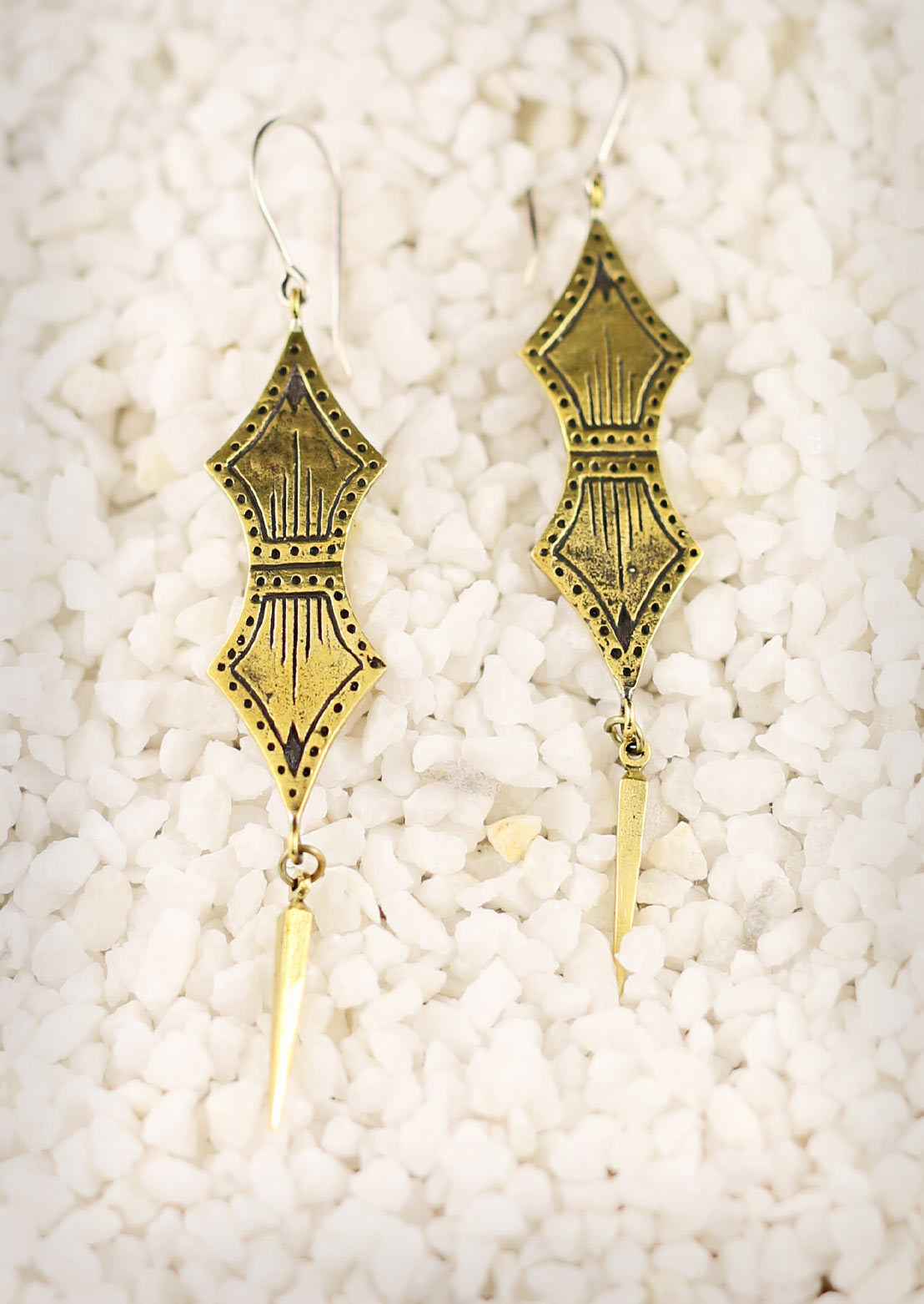A person wearing Primal Link Earrings with a subtle tribal design, featuring double spade-shaped brass ornaments and sterling silver hooks.