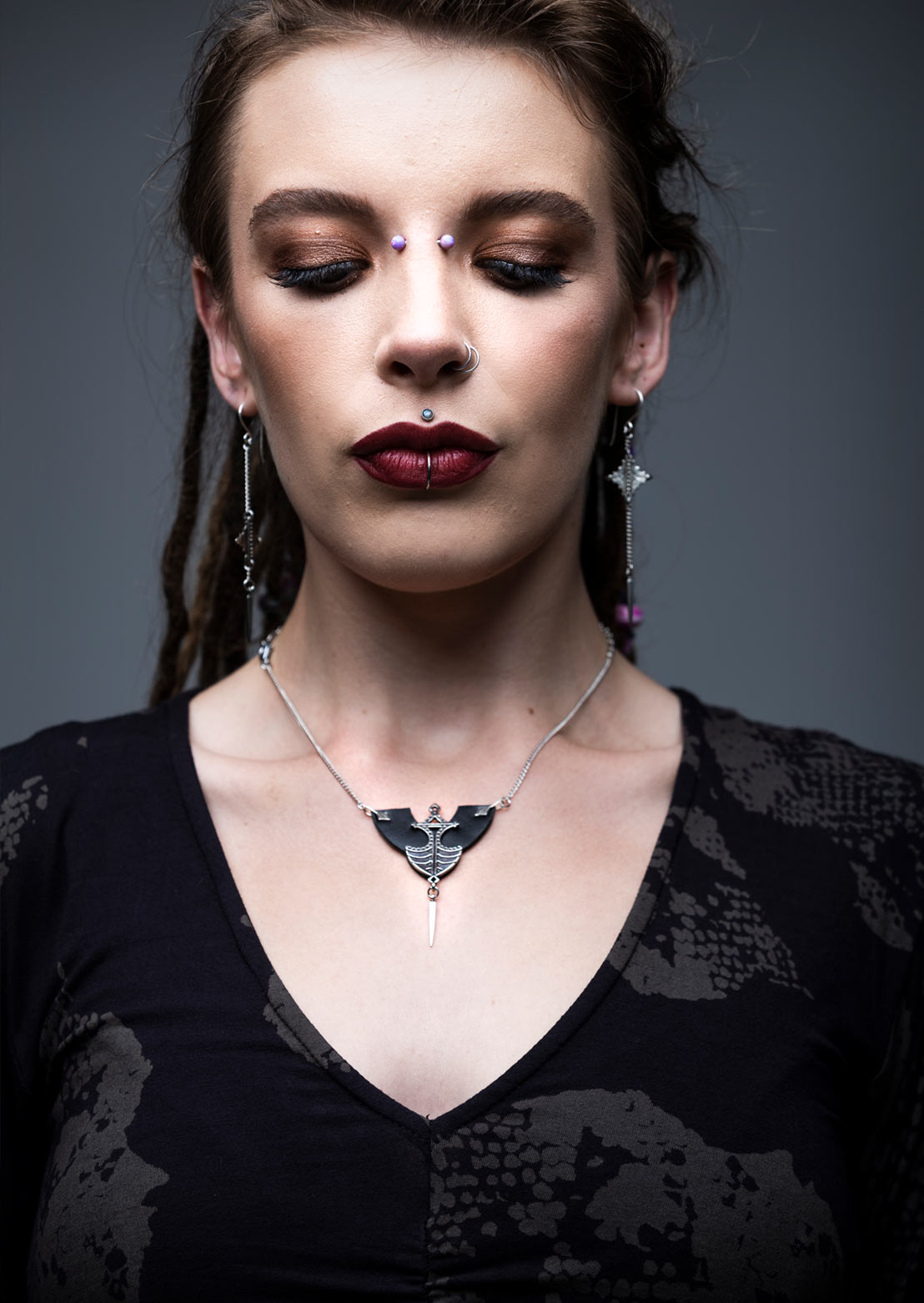 A close-up image of a woman wearing a tribal-style necklace with a leather half-spade shape and a pendulum tip, complemented by matching earrings.