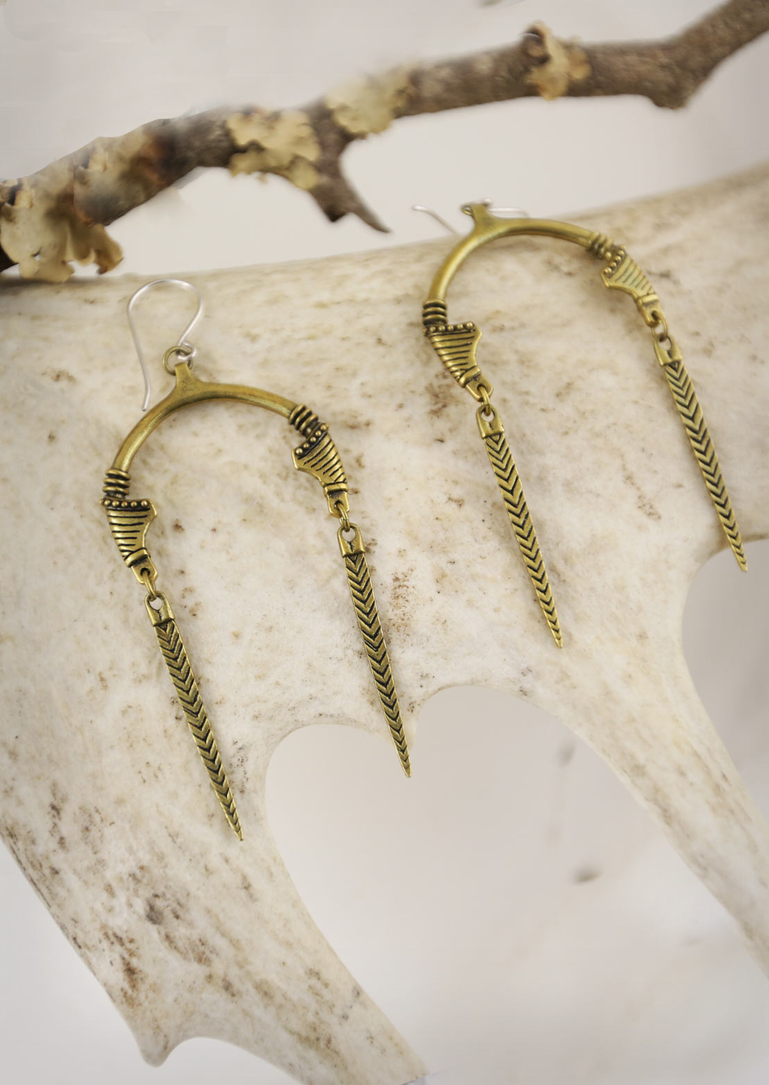 A pair of gold-tone Sahara earrings with an open U-shape and tribal marks design, displayed on a white antler.