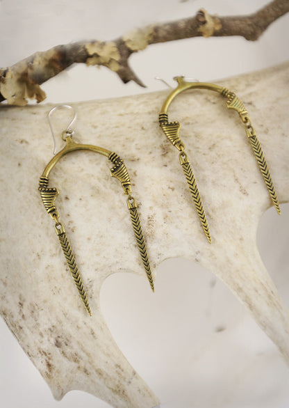 A pair of gold-tone Sahara earrings with an open U-shape and tribal marks design, displayed on a white antler.