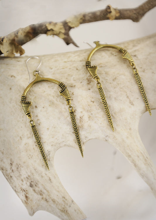 A pair of gold-tone Sahara earrings with an open U-shape and tribal marks design, displayed on a white antler.