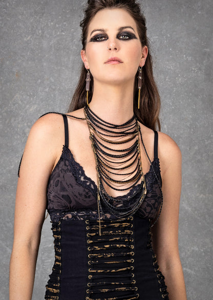 A person wearing a black faux leather necklace with brass chains and pouches, featuring a bold, tribal-inspired design.